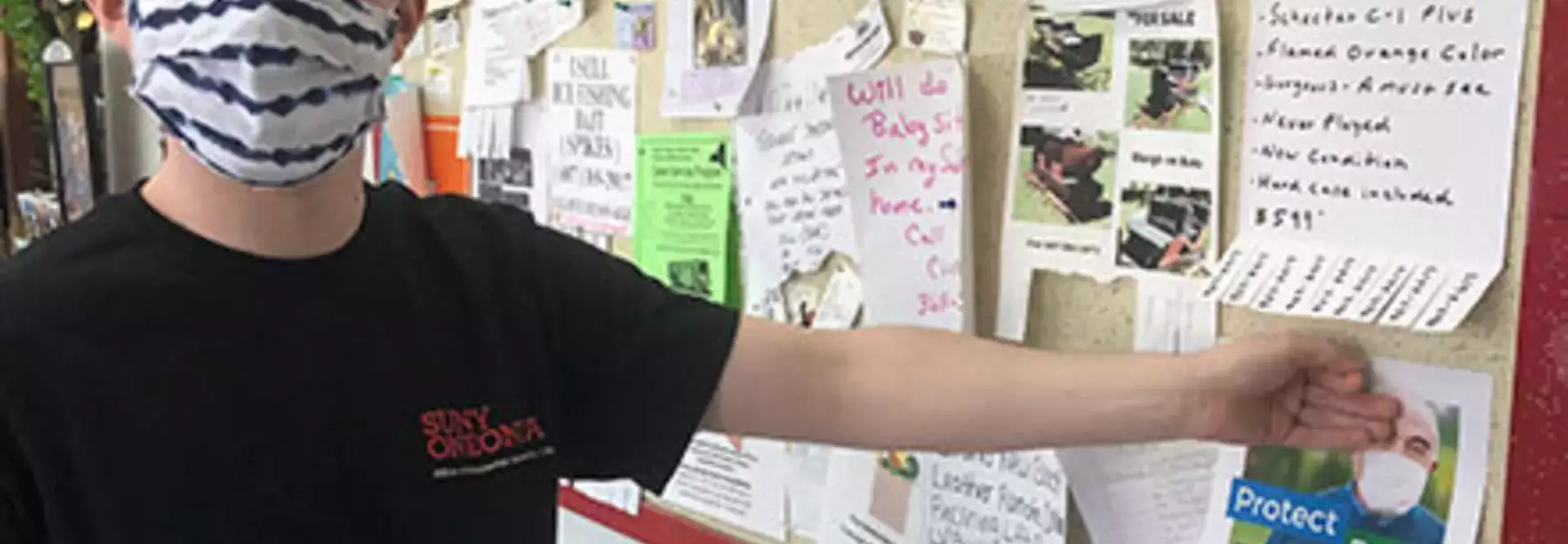 Student in mask posting COVID vaccination flyer on bulletin board