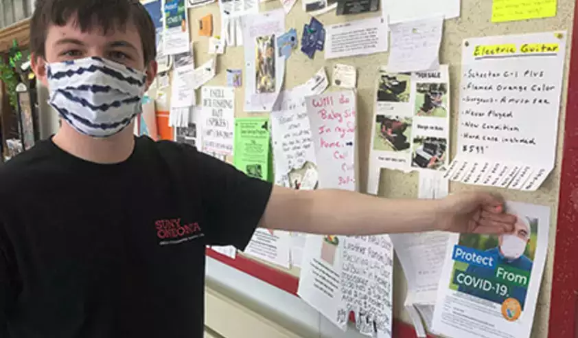 Student in mask posting COVID vaccination flyer on bulletin board
