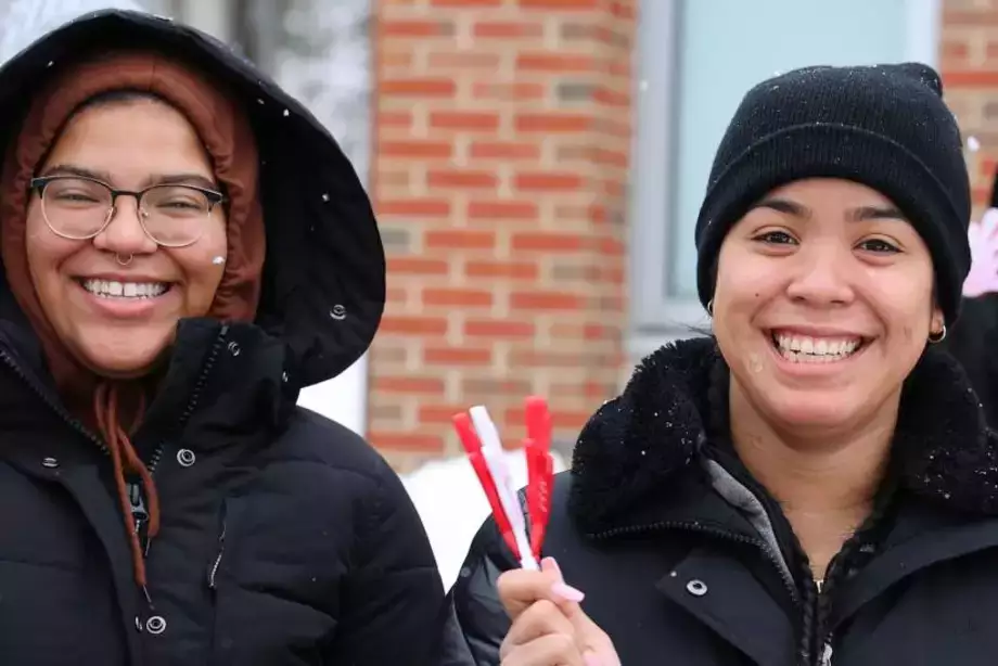 Two students smiling while holding clappers at the Pass Through the Pillars event. 