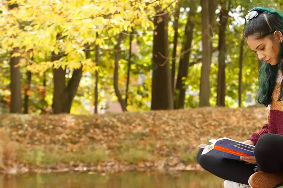 Person reading on a rock next to SUNY Oneonta's Hunt Union Pond