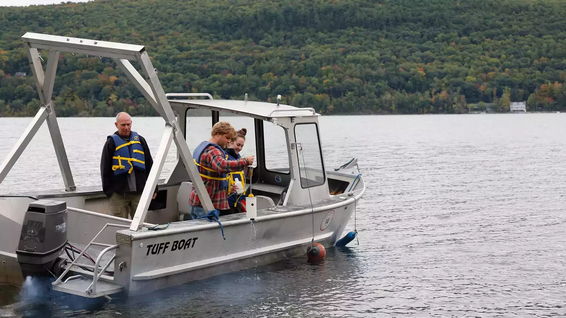 Three people on a boat collecting data from Otsego Lake